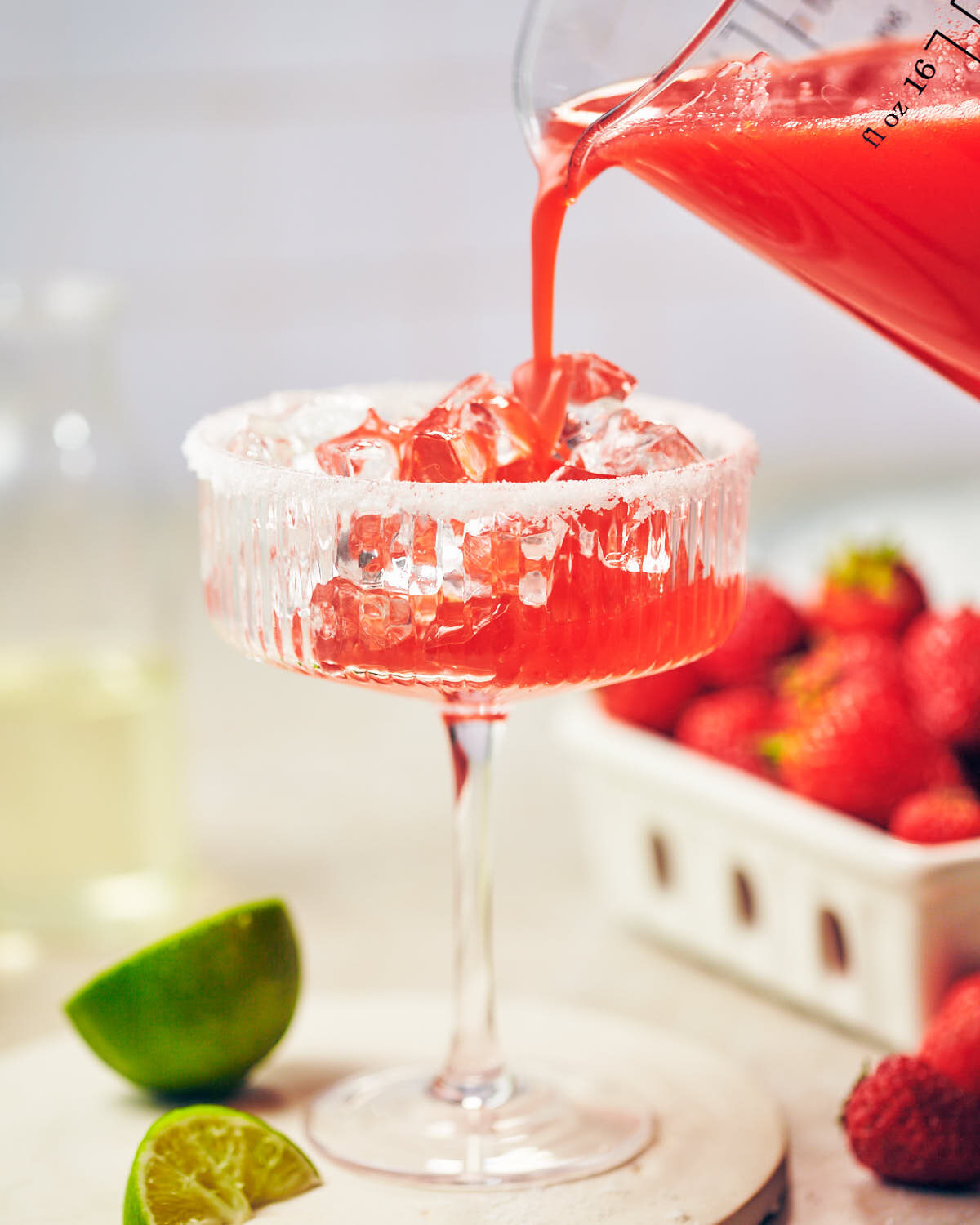 Pouring blended Strawberry Jalapeno Margarita over cocktail glass filled with ice.