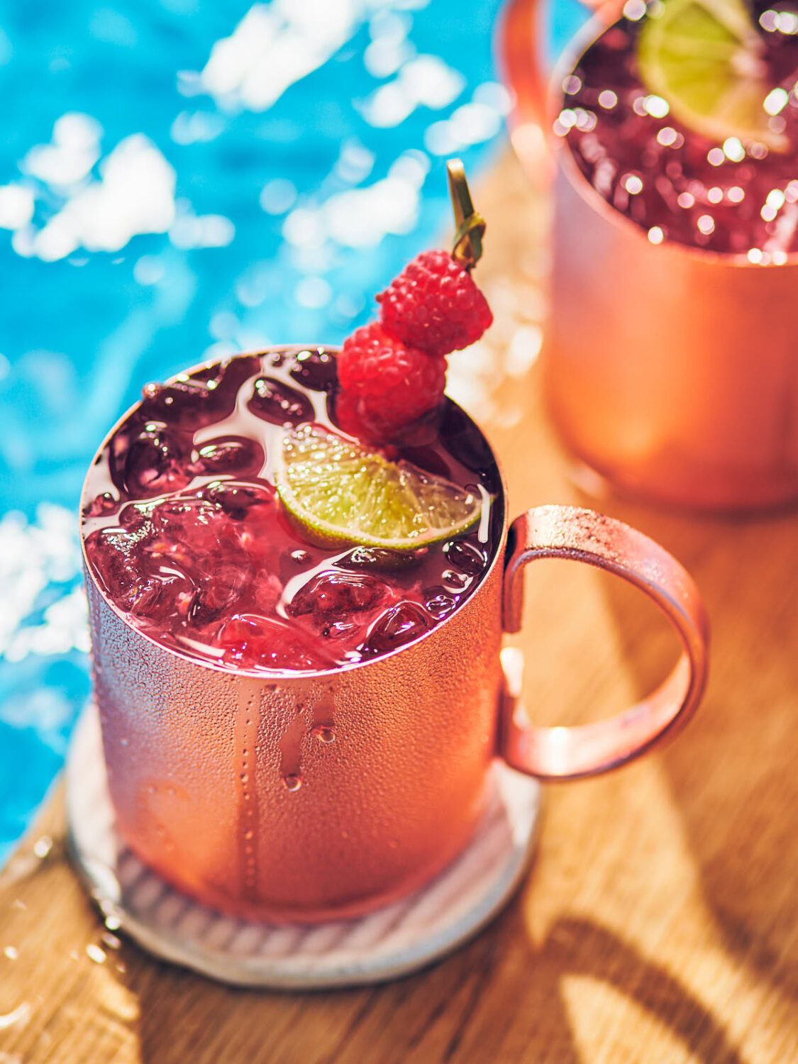 Raspberry Mule in a copper mug filled with ice, topped with raspberries and lime.