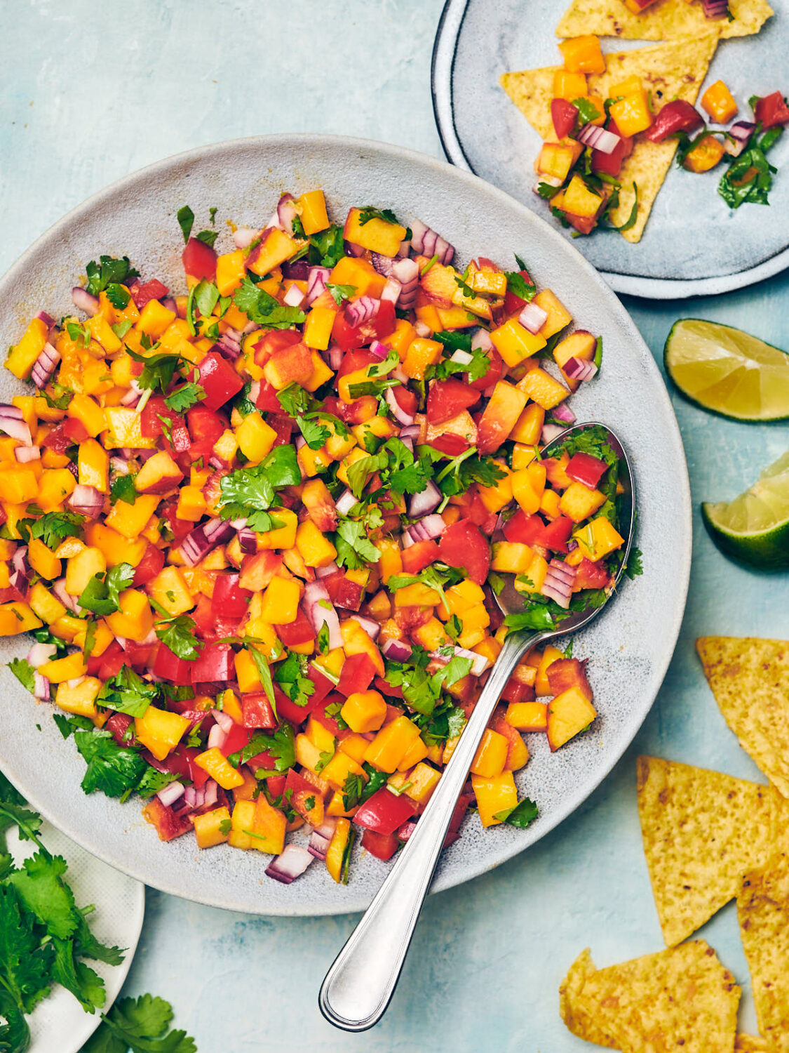 Peach Mango Salsa in a serving bowl with tortilla chips, limes, and cilantro.