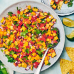 Peach Mango Salsa in a serving bowl with tortilla chips, limes, and cilantro.