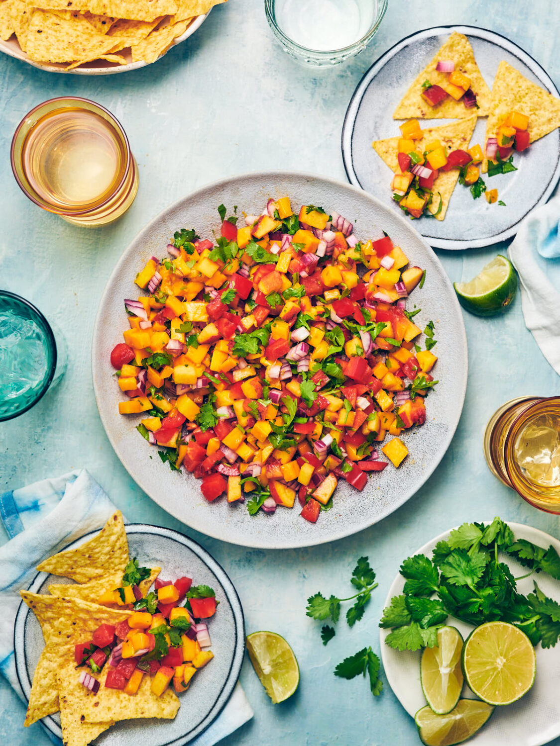Peach Mango Salsa being served with tortilla chips, fresh limes, cilantro, and drinks.