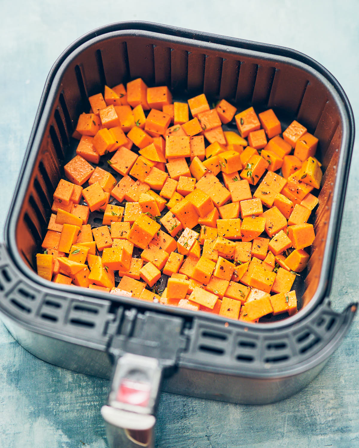 Seasoned cubes of butternut squash spread out in an air fryer basket.