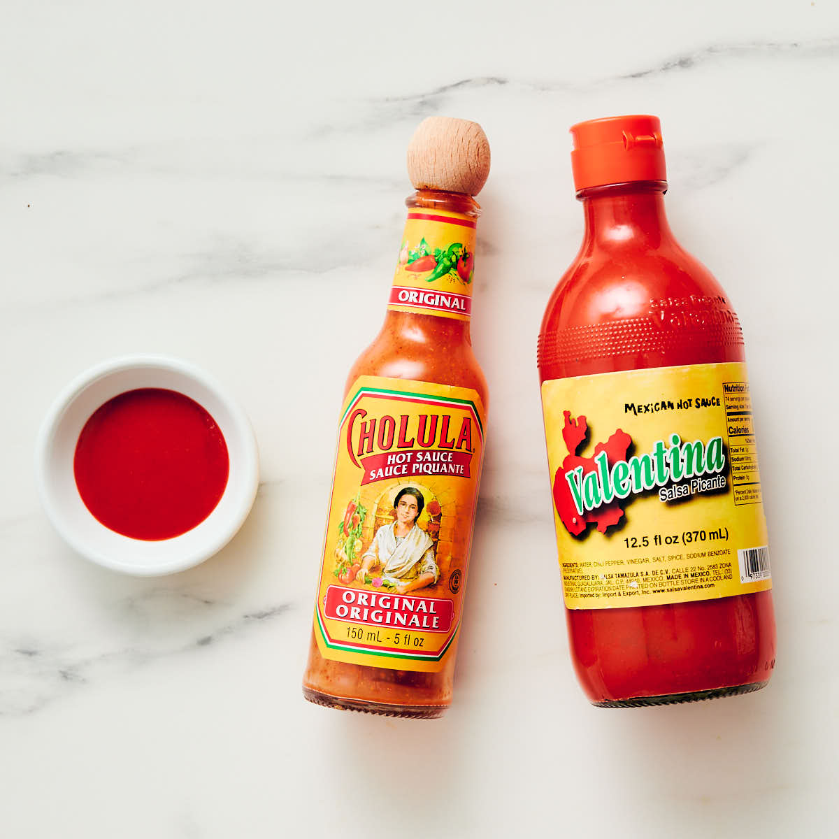 Cholula and Valentina hot sauce bottles with a small bowl of Mexican hot sauce.