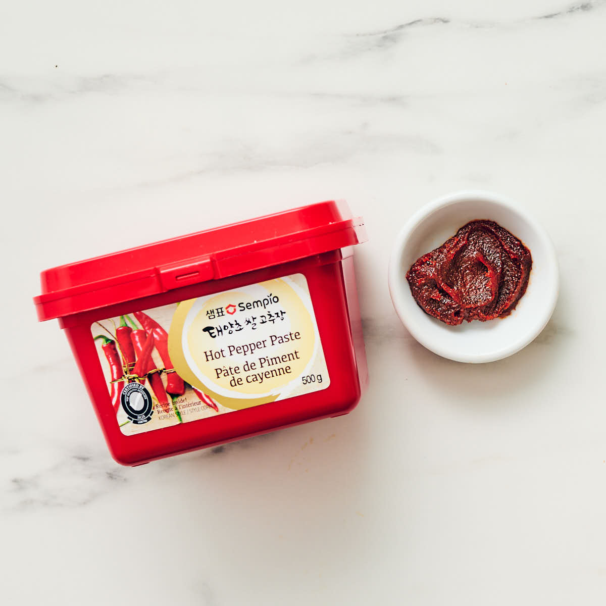 Gochujang (Korean chili paste) in a red package with a small bowl of paste scooped out.