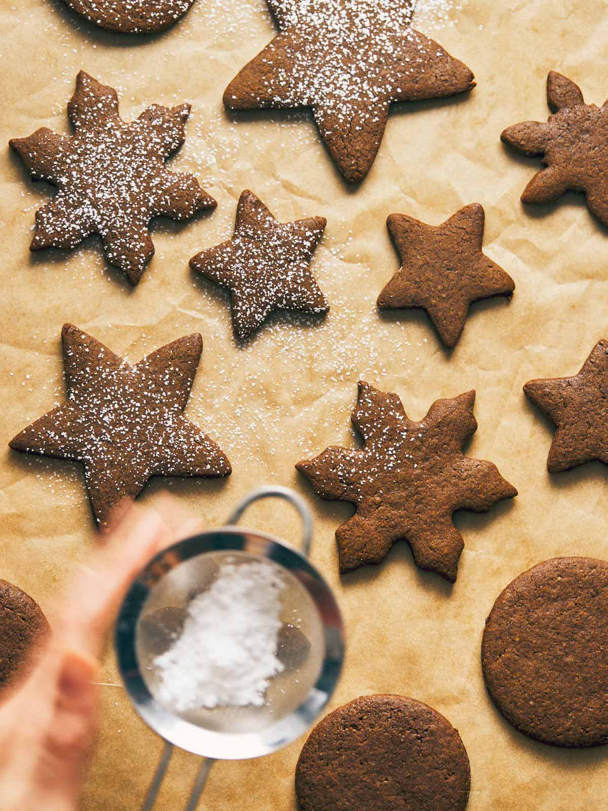 Vegan gingerbread cookies being dusted with powdered sugar.
