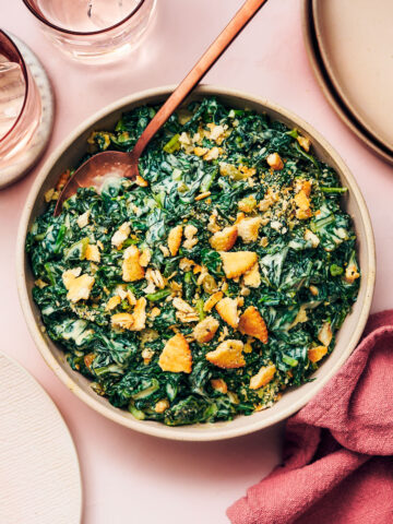 Easy vegetarian Creamed Kale in a serving bowl with a spoon on a dining table.