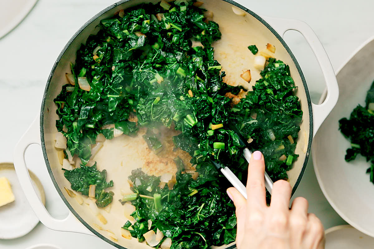 Removing cooked kale from a pan with kitchen tongs.