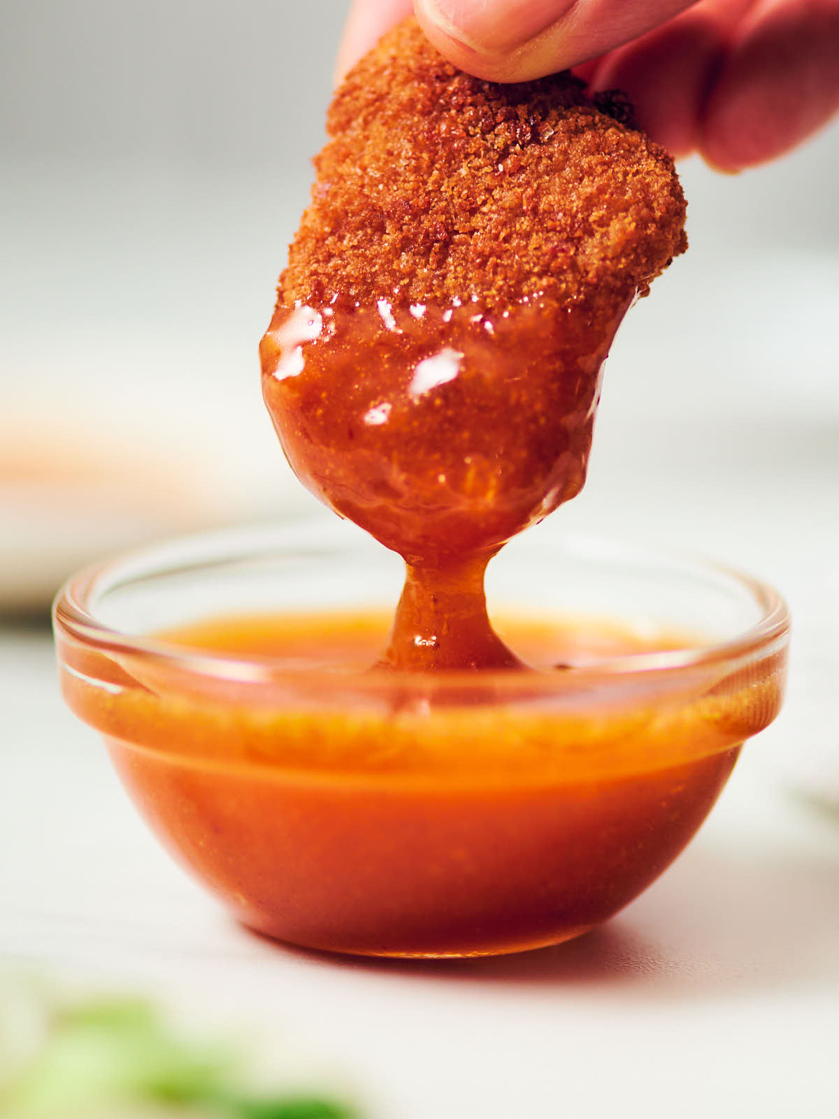 Plant-based chicken nugget being dipped in honey sriracha sauce.