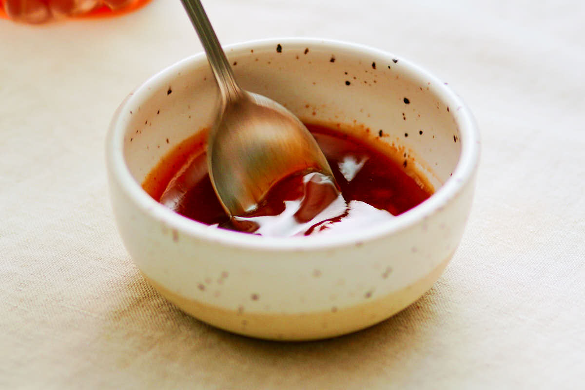 Mixing maple sriracha sauce in bowl with spoon.