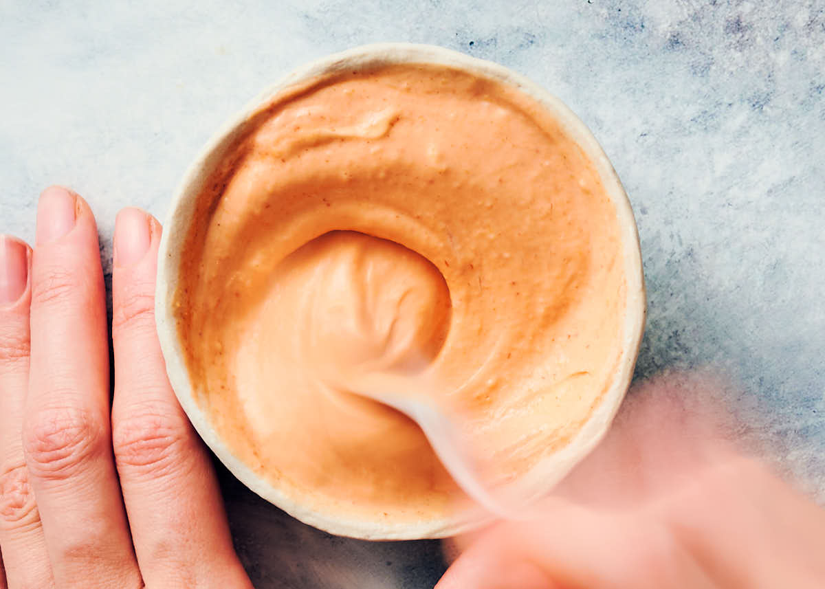Stirring sriracha aioli ingredients together in a small bowl with spoon.