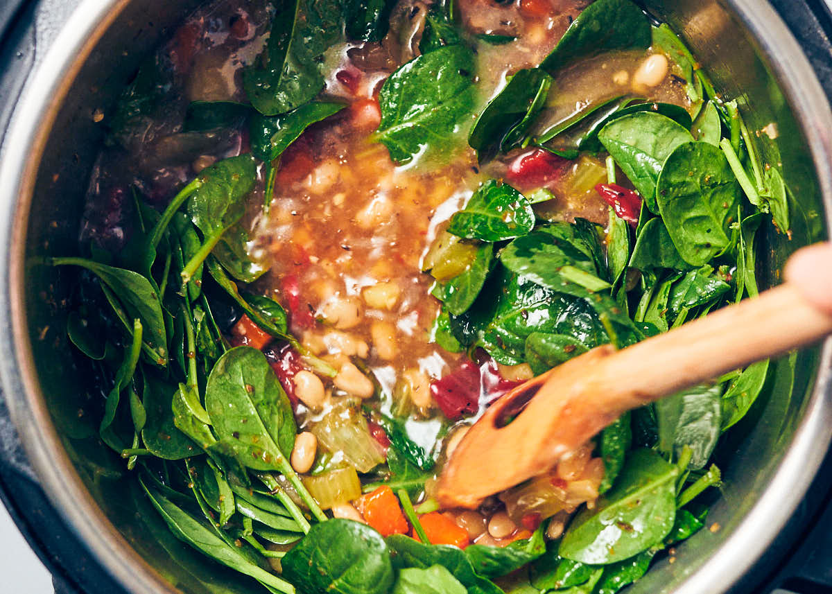 A wooden spoon stirring spinach into Instant Pot Bean Soup.