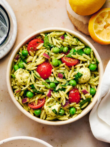Vegetarian Orzo Pesto Salad with tomatoes, peas, and cheese in a bowl.