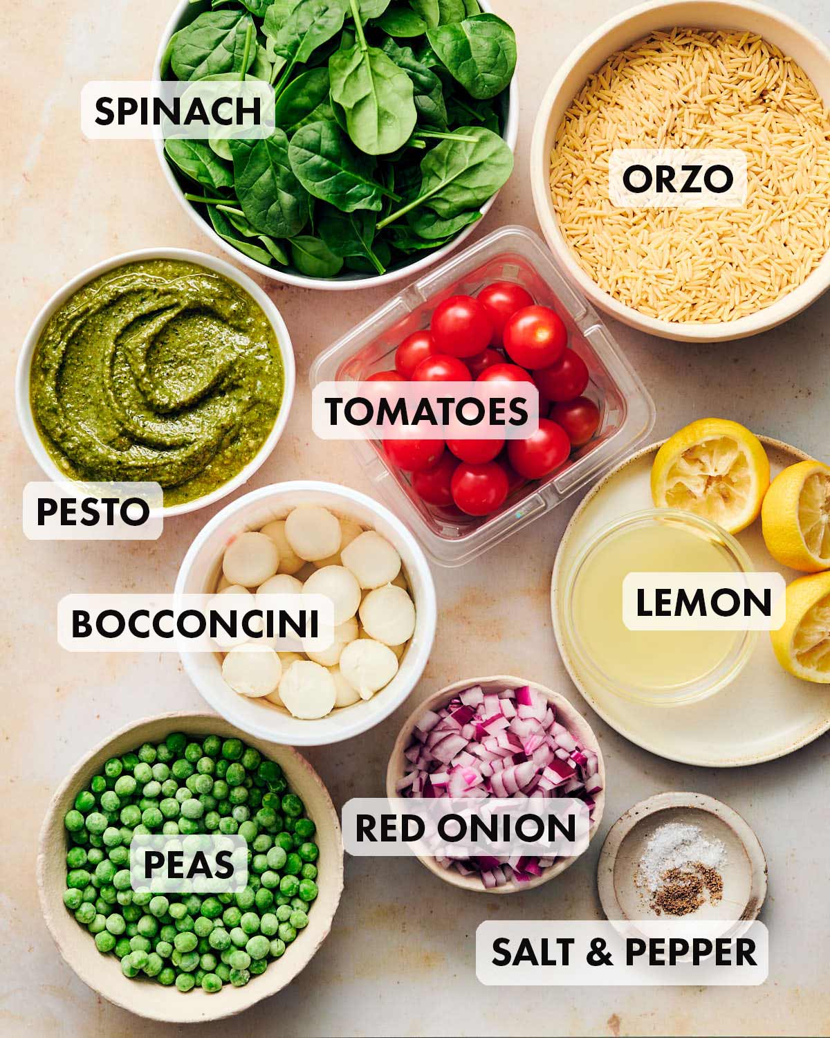 Ingredients to make Orzo Pesto Salad including red onion, lemon, spinach, and tomatoes.