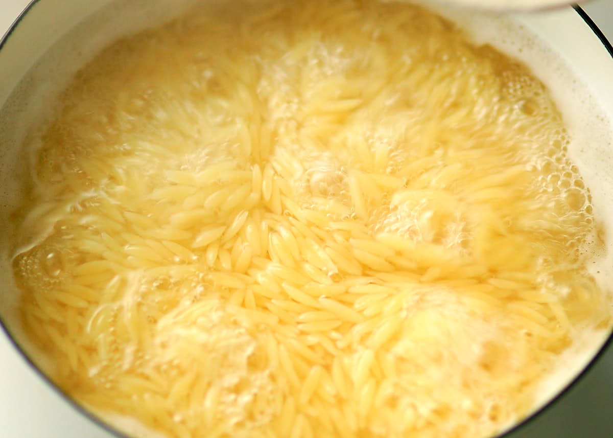Dried orzo pasta cooking in a pot of boiling salted water.