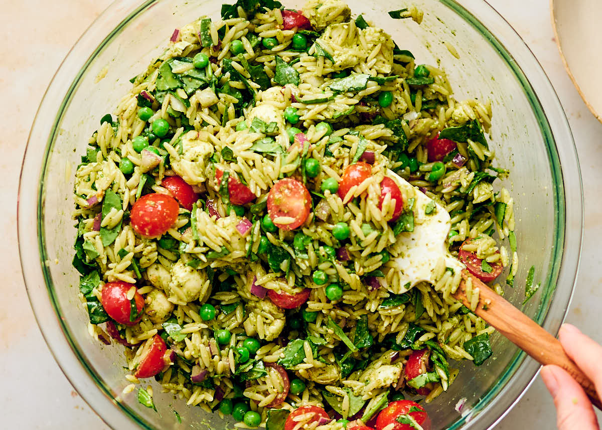 Tossing vegetarian Orzo Pesto Salad in a bowl before serving.