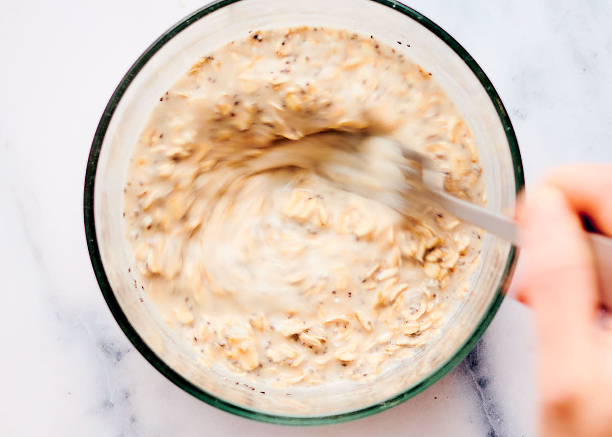 Mixing ingredients together for overnight oats in a glass bowl.