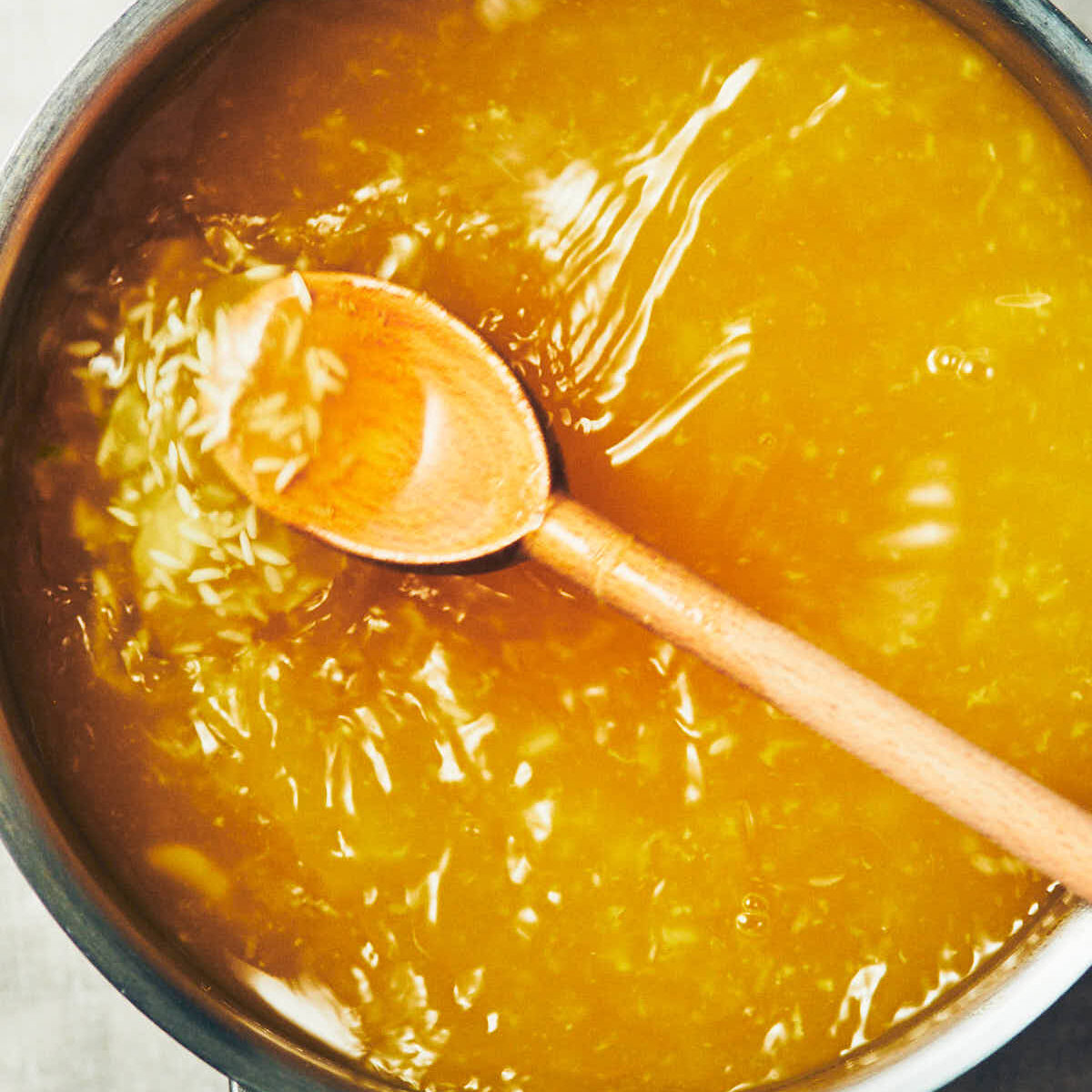 A spoon stirring vegetable stock, ginger, and garlic, into a pot of rice for congee.