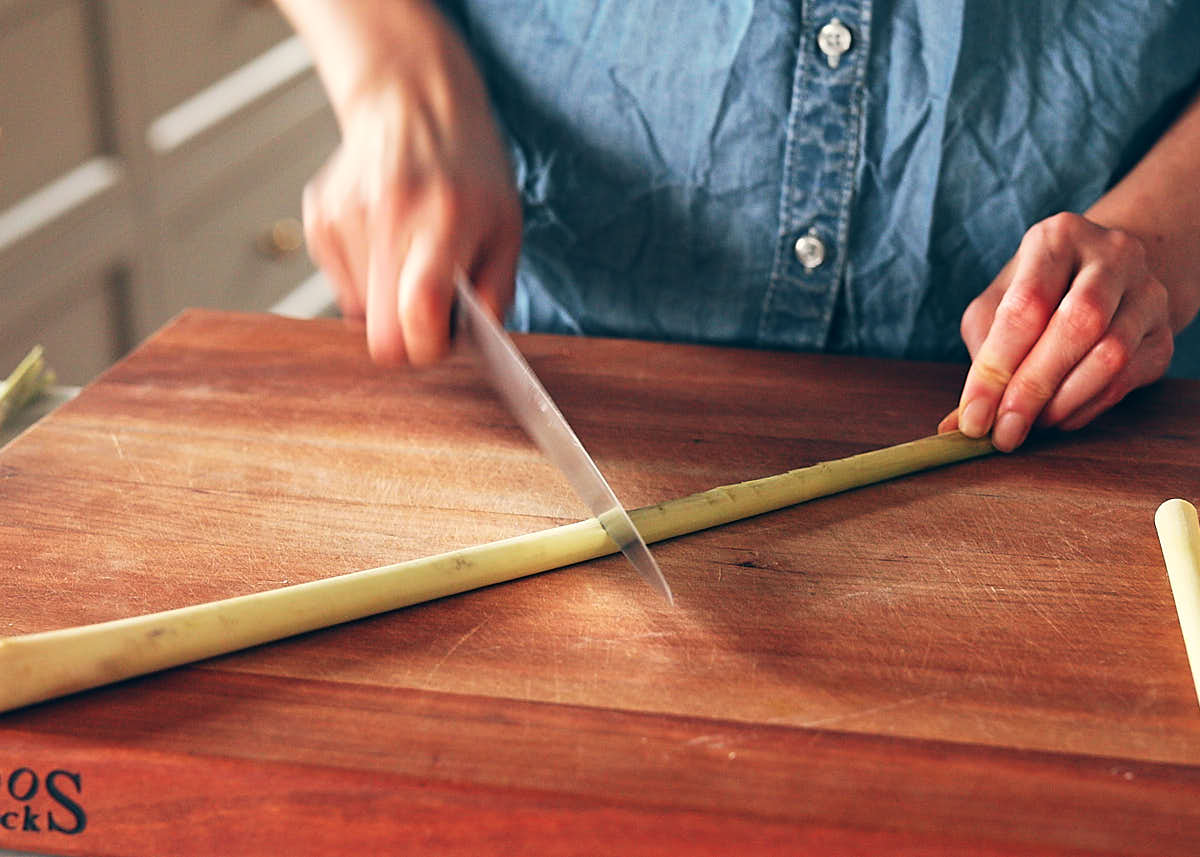 Lemongrass on a cutting board being pounded with a knife to release the oils for vegan tom yum.