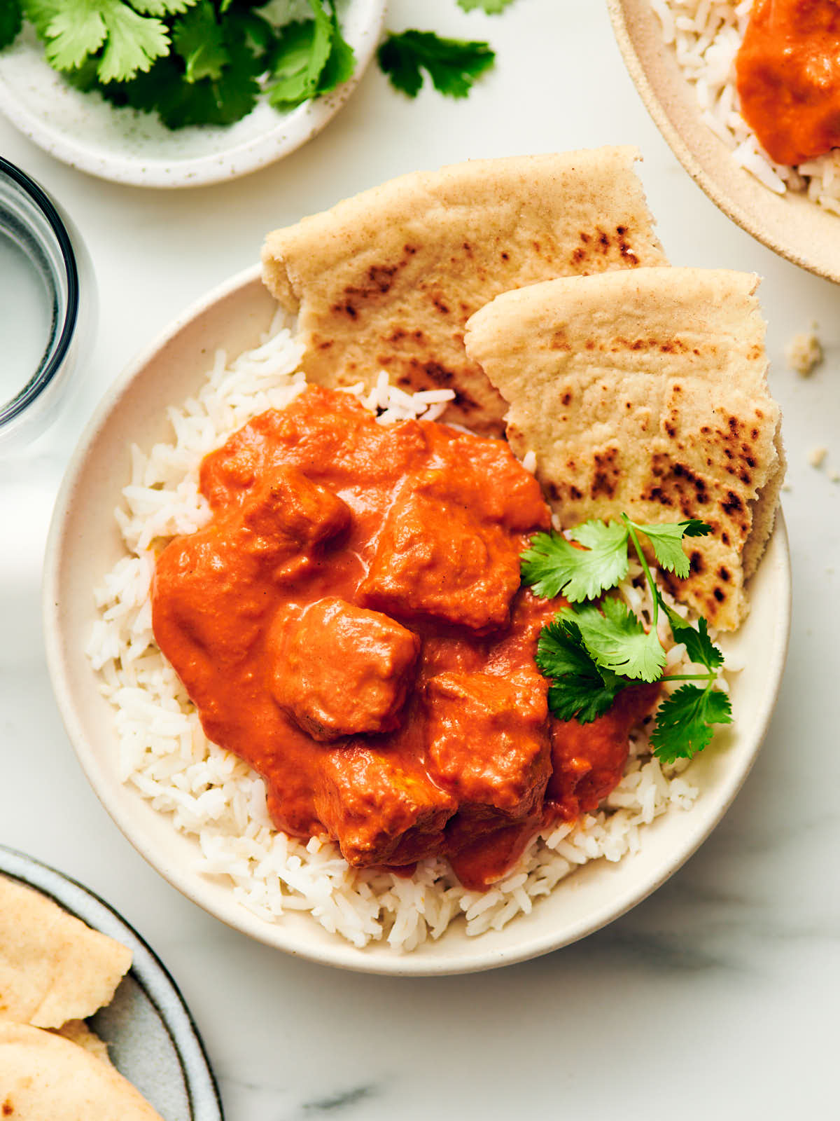 Vegetarian Butter Chicken in a bowl with rice, naan, and cilantro.