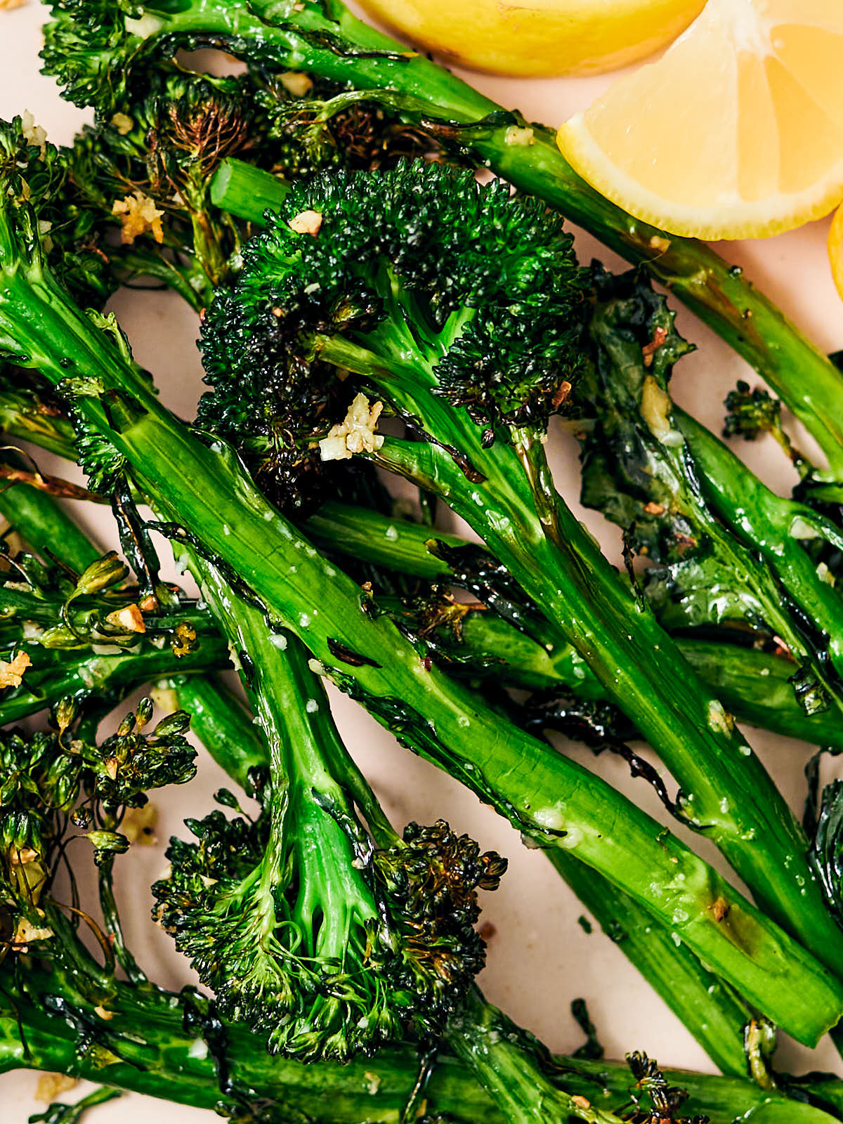 Air fryer broccolini on a dinner plate with lemon wedges.