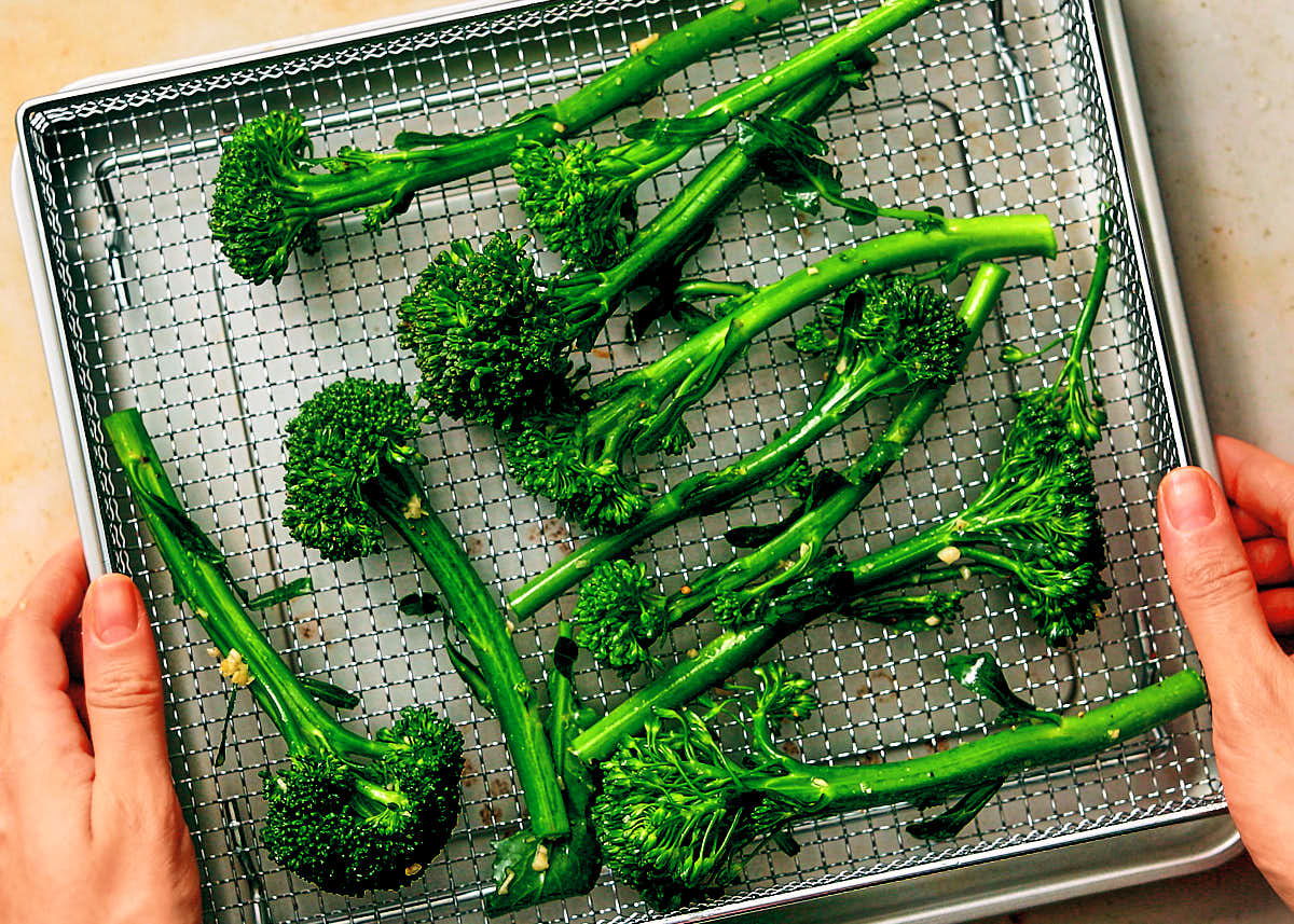 Seasoned broccolini in an air fryer basket about to be baked.