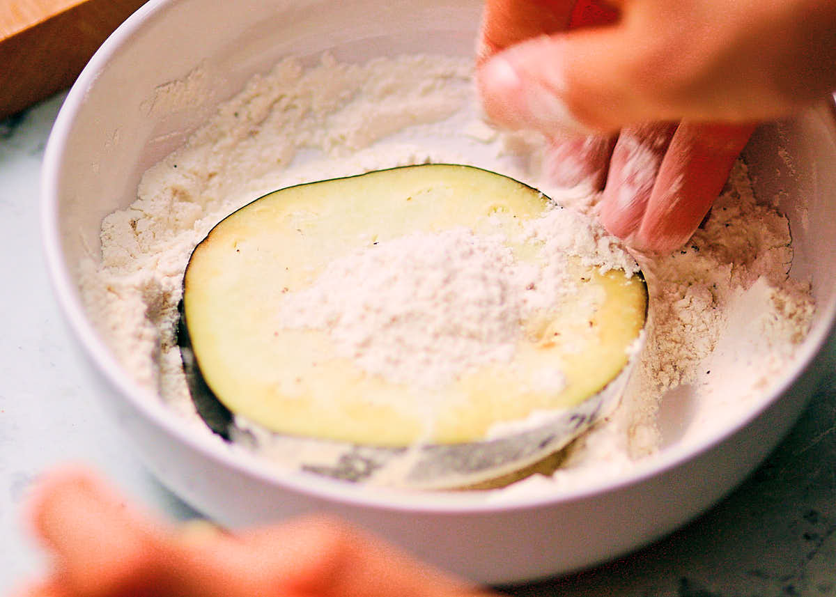 Dipping sliced eggplant in a bowl of flour to make eggplant parmesan.