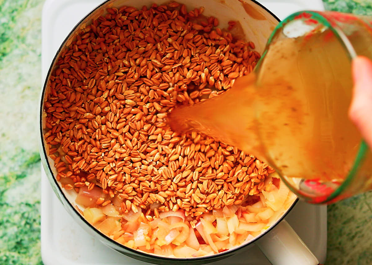 Pearled farro in a pot with vegetable broth being poured on top to cook until tender.