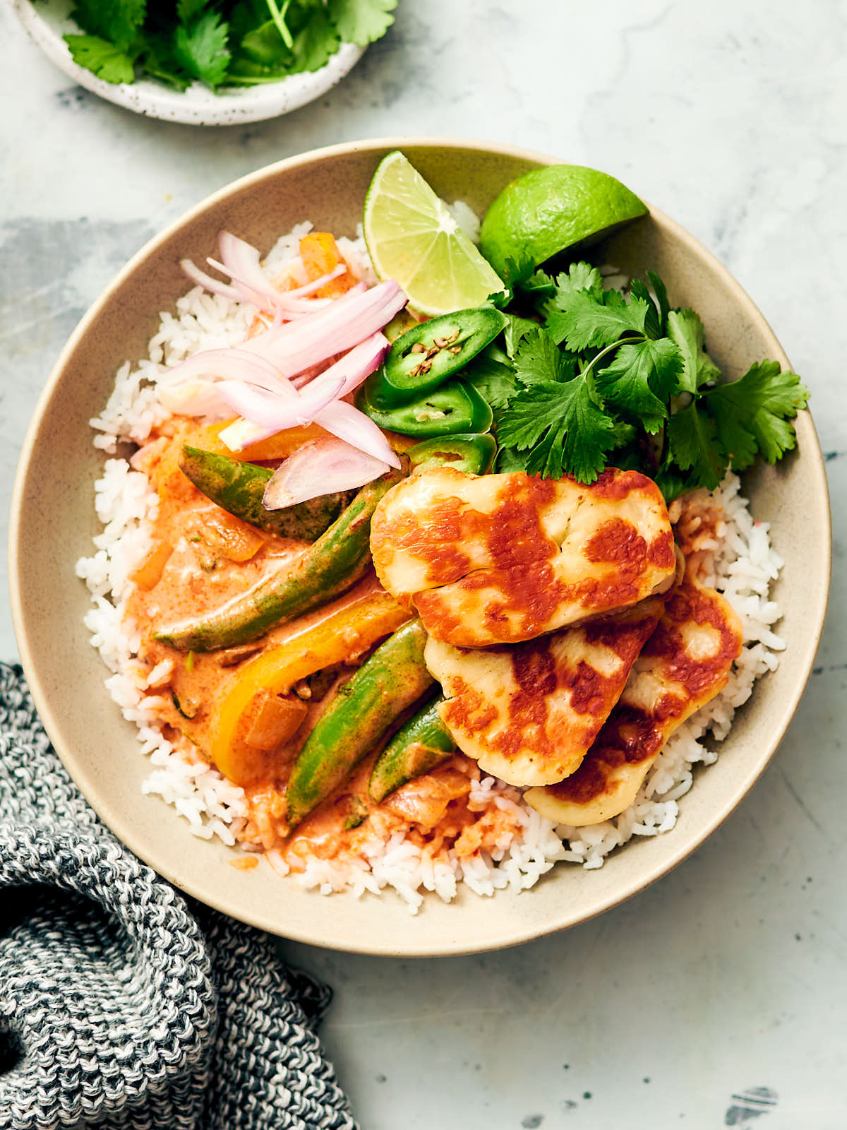 Easy Halloumi Curry spooned over a bowl of rice with fresh herbs and limes.