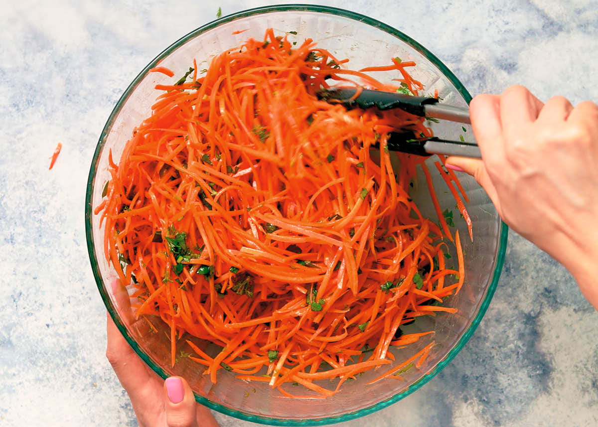 Tossing carrots and herbs with the dressing to make raw carrot salad.
