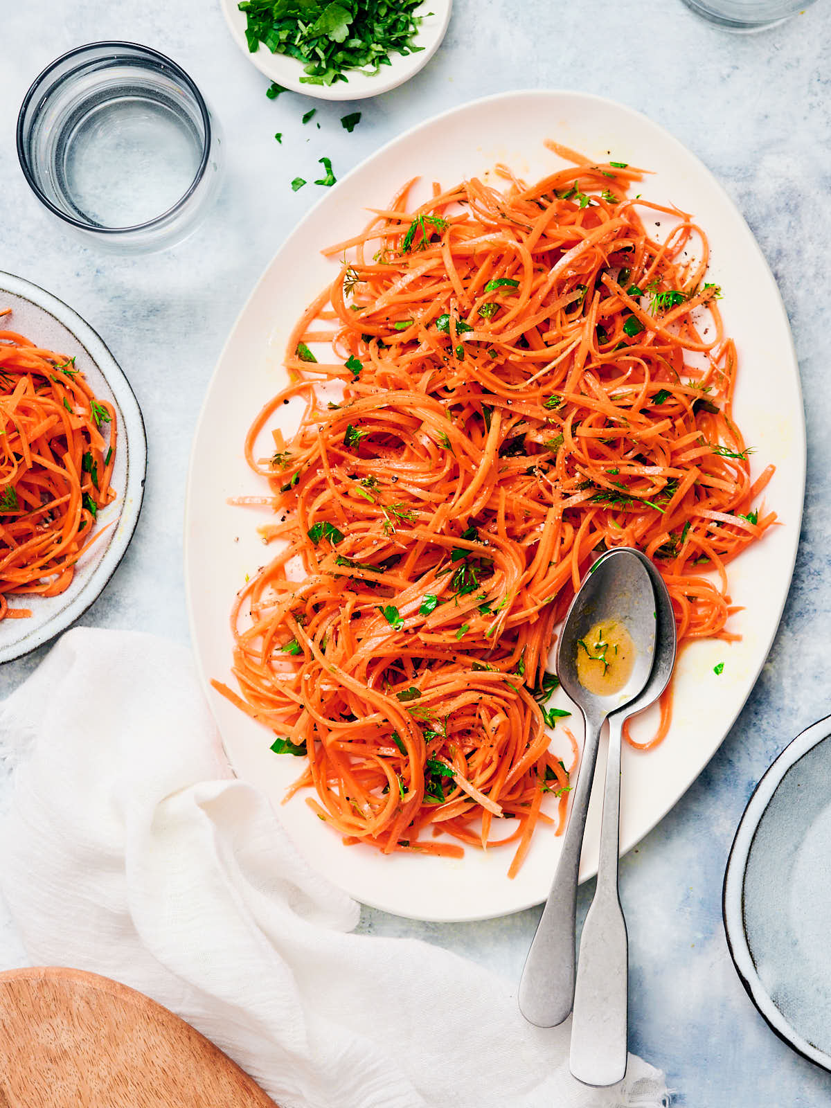 Raw carrot salad on an oval serving plate with serving spoons.