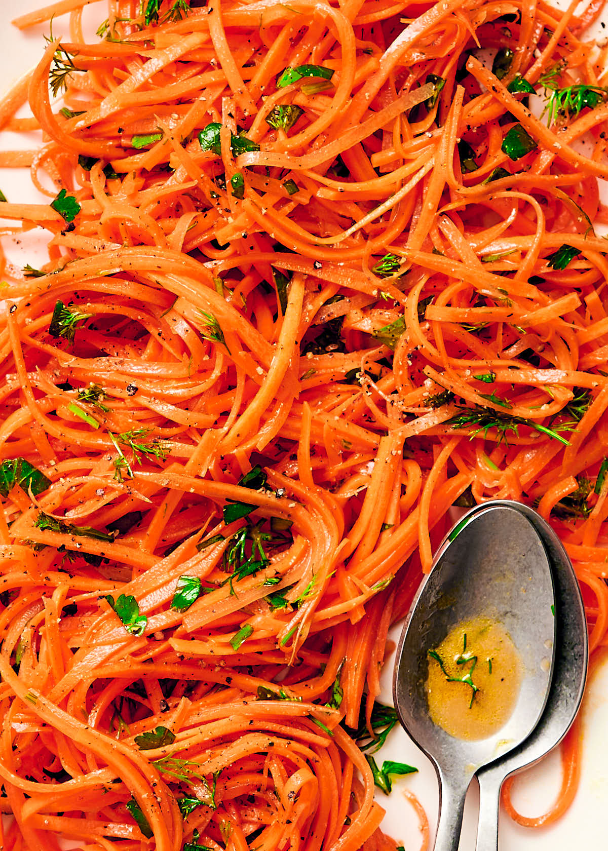 Close up of raw carrot salad on a plate topped with parsley and dill.
