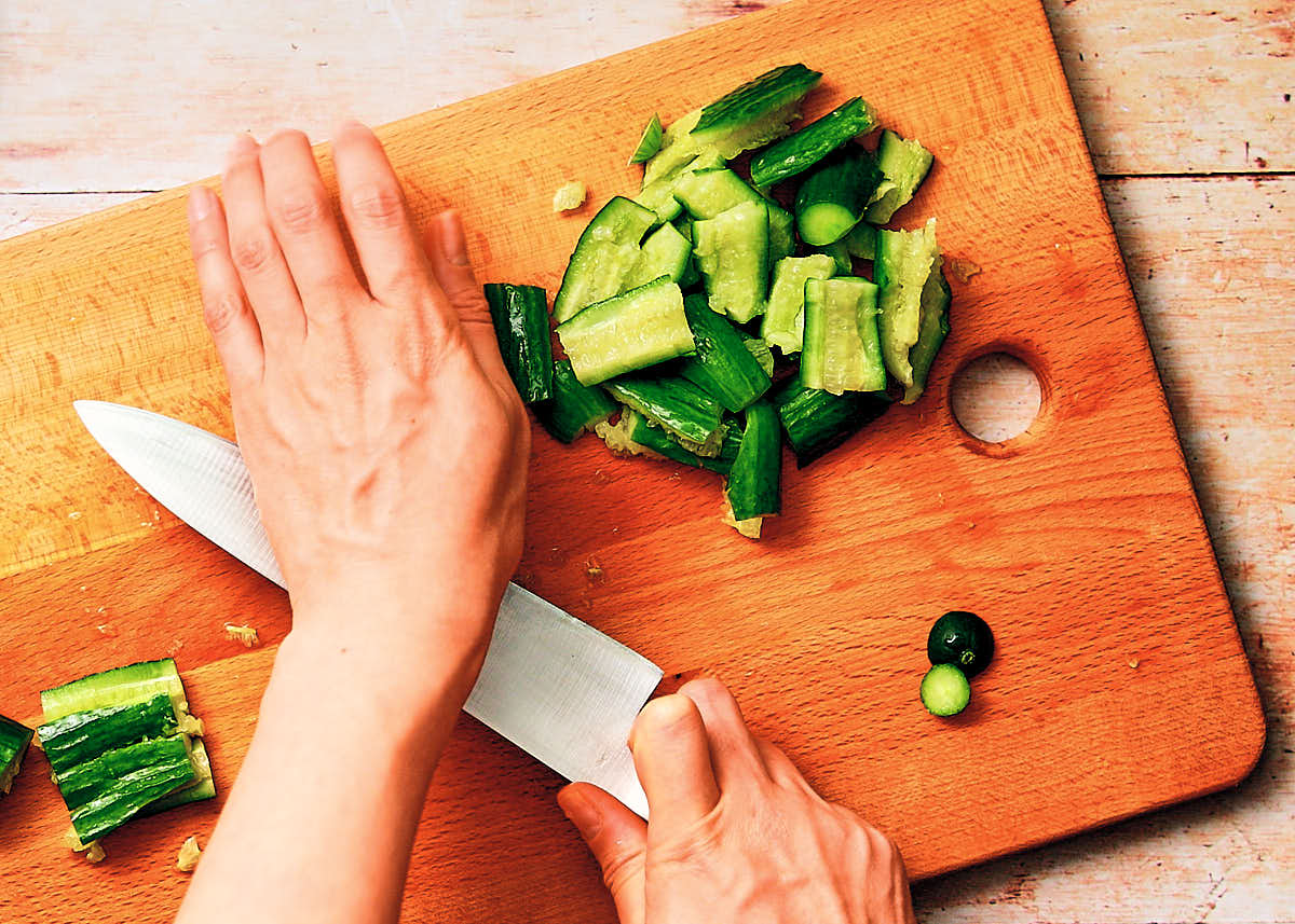 Smashing cucumbers on a cutting board with a knife.