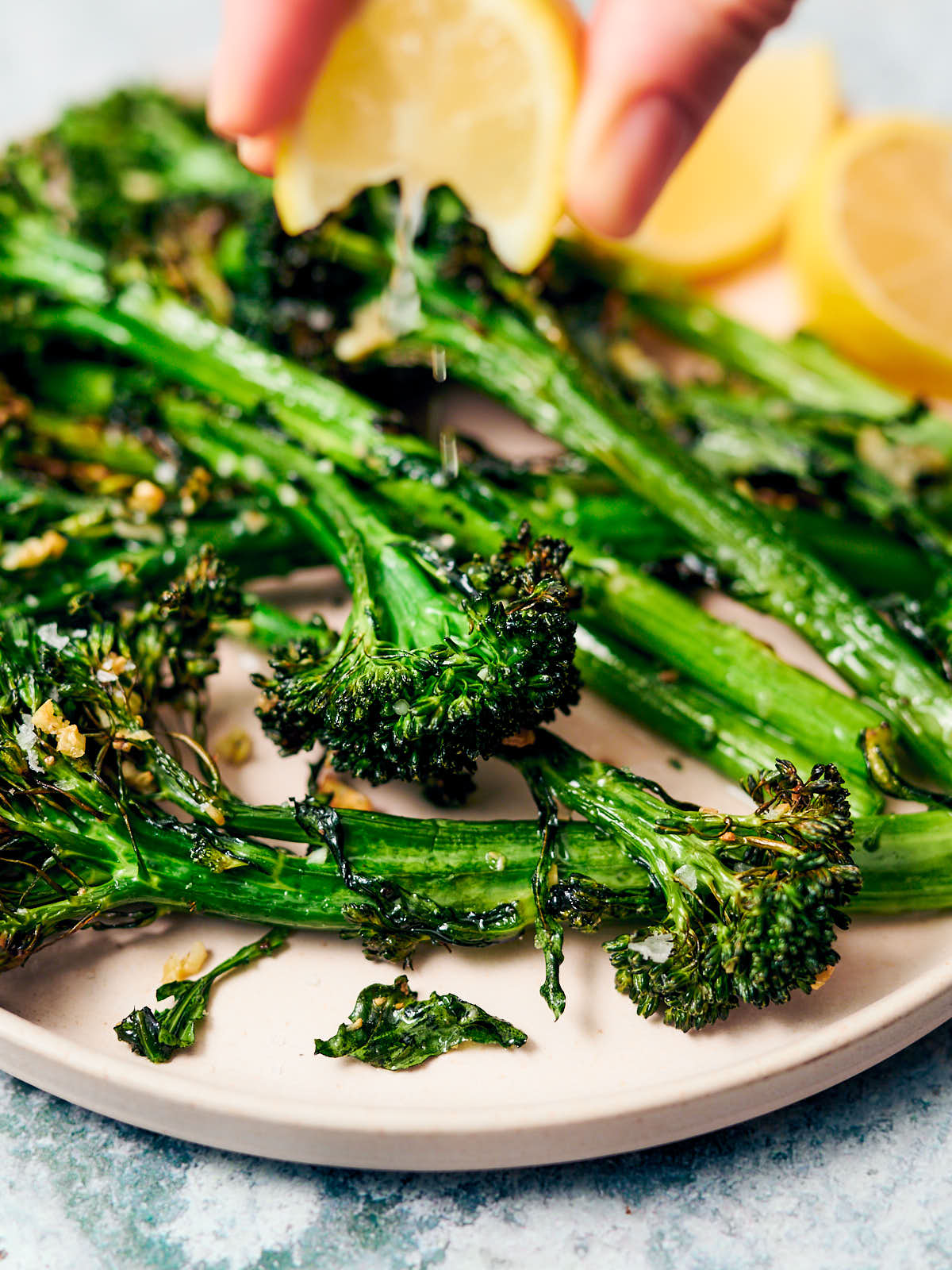 Squeezing fresh lemon over air fried broccolini on a plate.