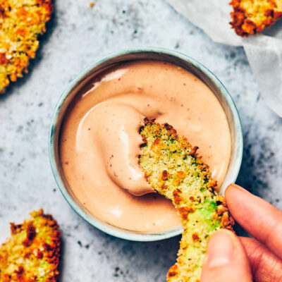A crispy avocado fry being dipped into vegan chipotle mayo