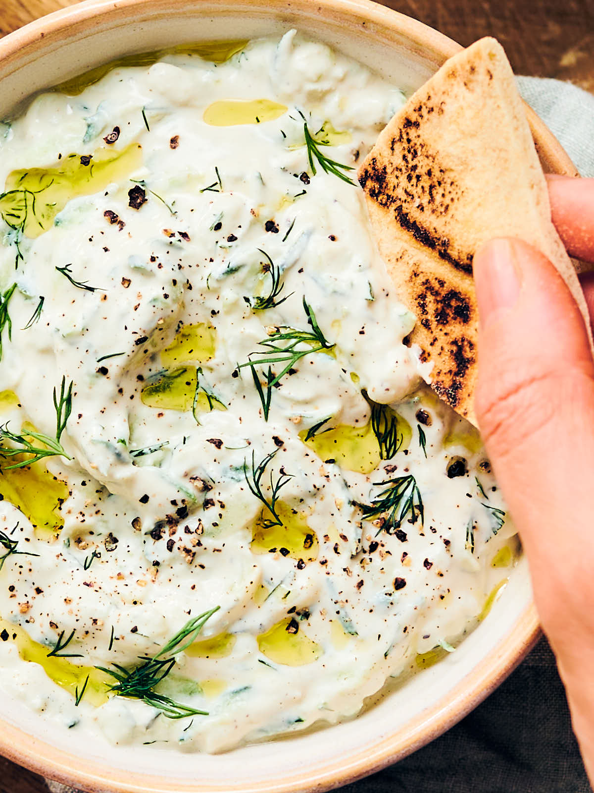 Pita being dipped into a bowl of cashew based vegan tzatziki topped with dill.