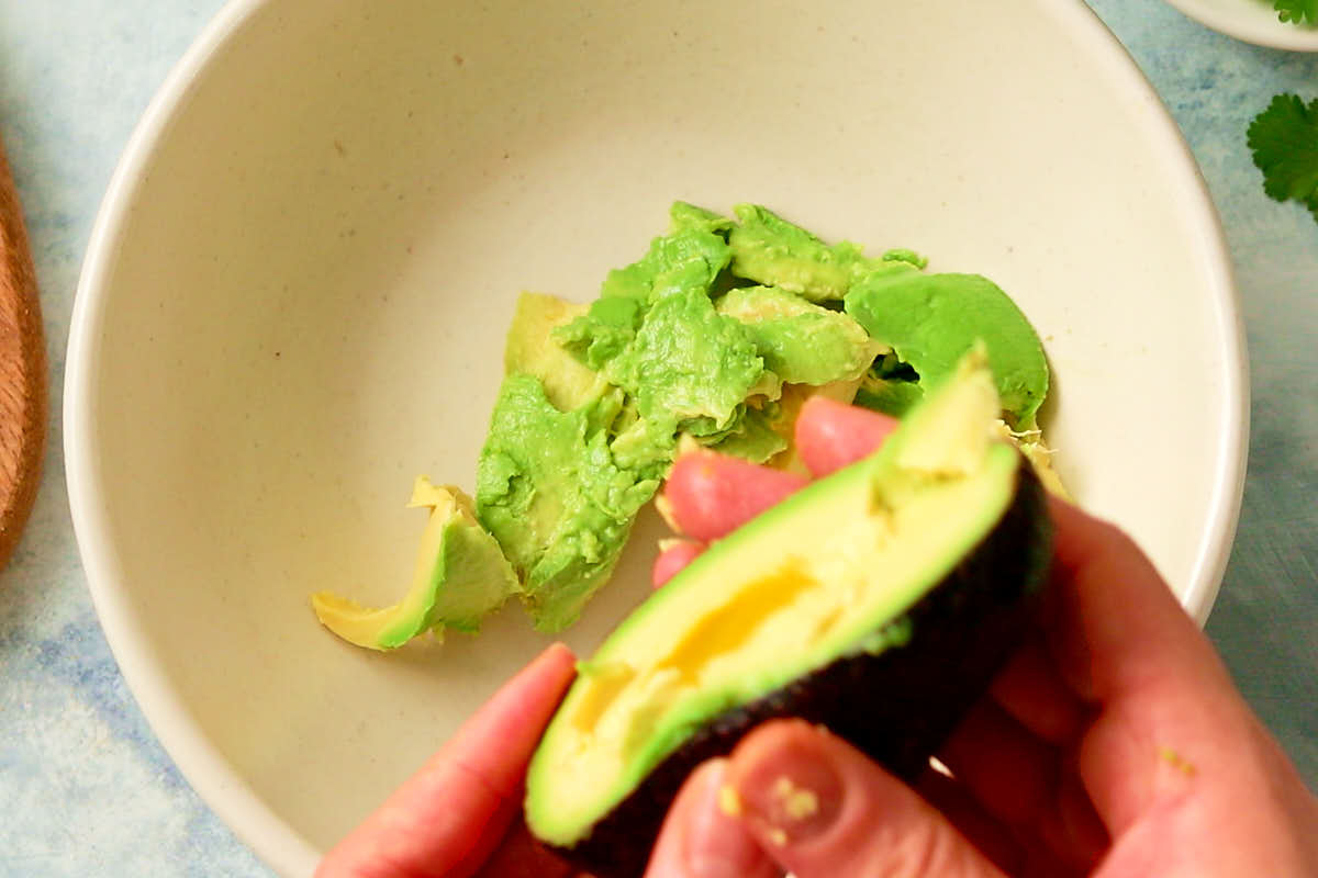 Scooping avocado flesh into a bowl for vegan guacamole.