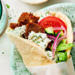 A Greek-inspired Vegan Gyros with tzatziki and tomato on a dinner plate.