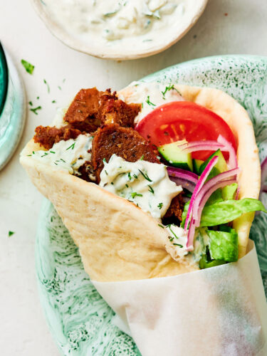 A Greek-inspired Vegan Gyros with tzatziki and tomato on a dinner plate.