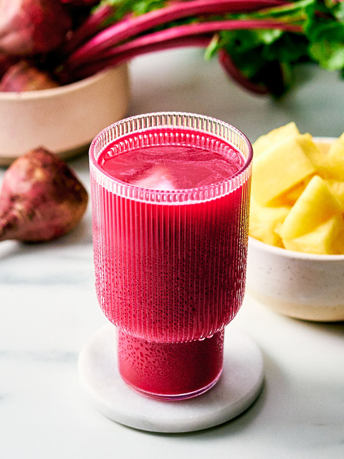 Beet Pineapple Juice in a glass with fresh pineapple and beet in bowls.