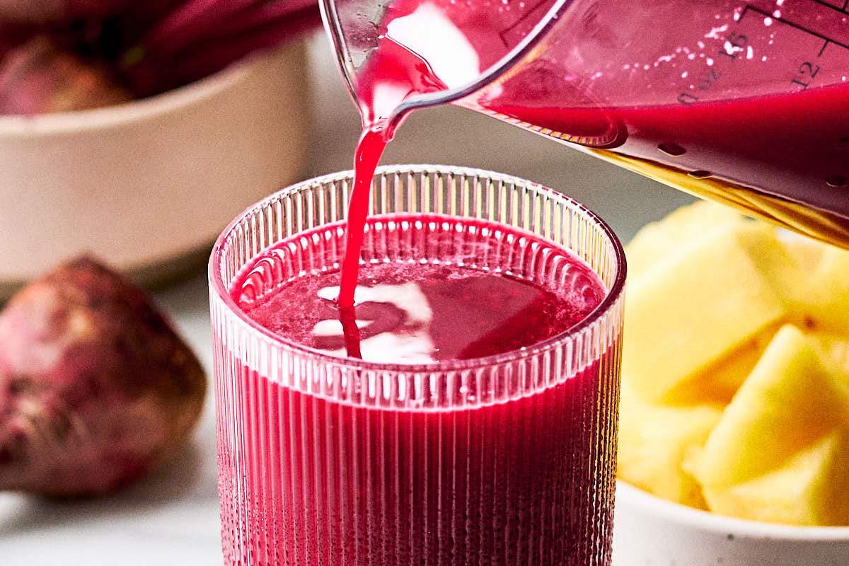Beet and pineapple juice being poured into glasses for serving.