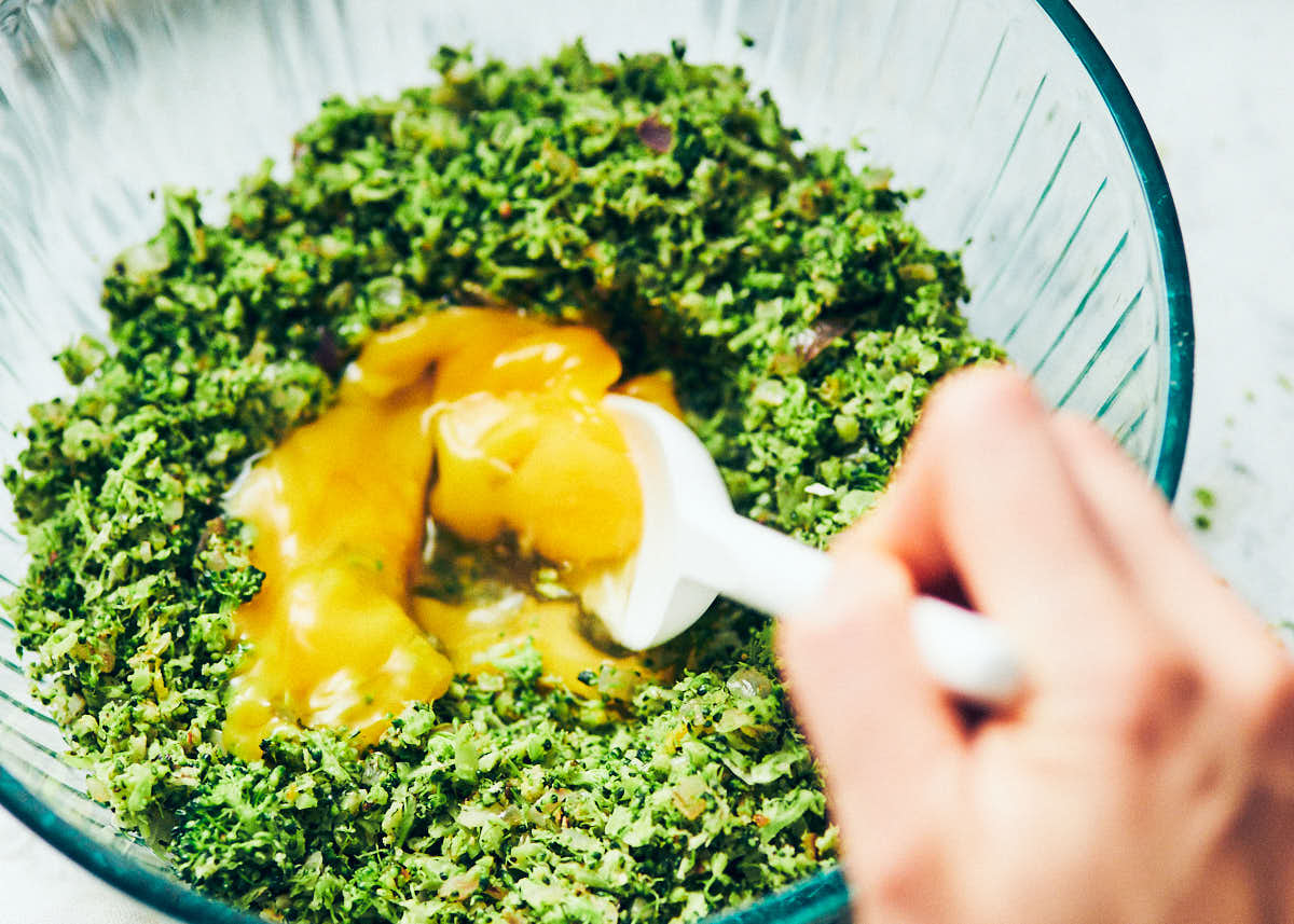 Stirring eggs into broccoli tots mixture in a glass bowl.