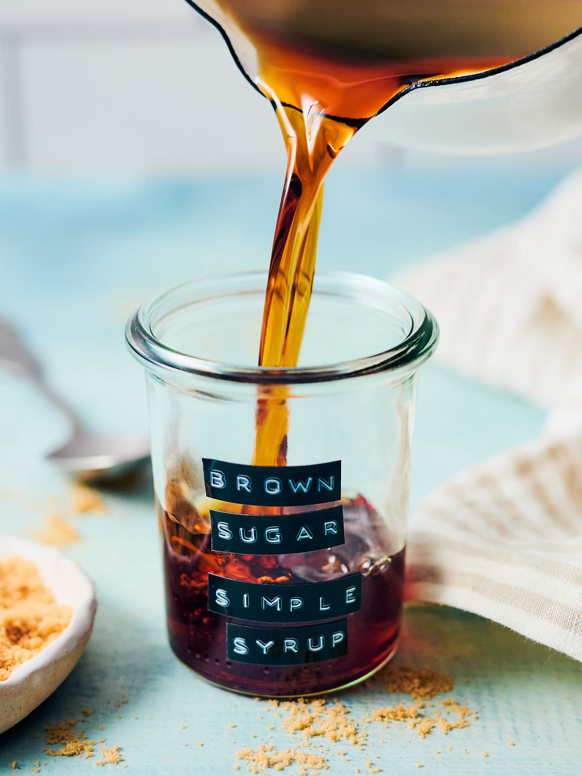 Brown sugar simple syrup being poured out of a saucepan into a glass jar.