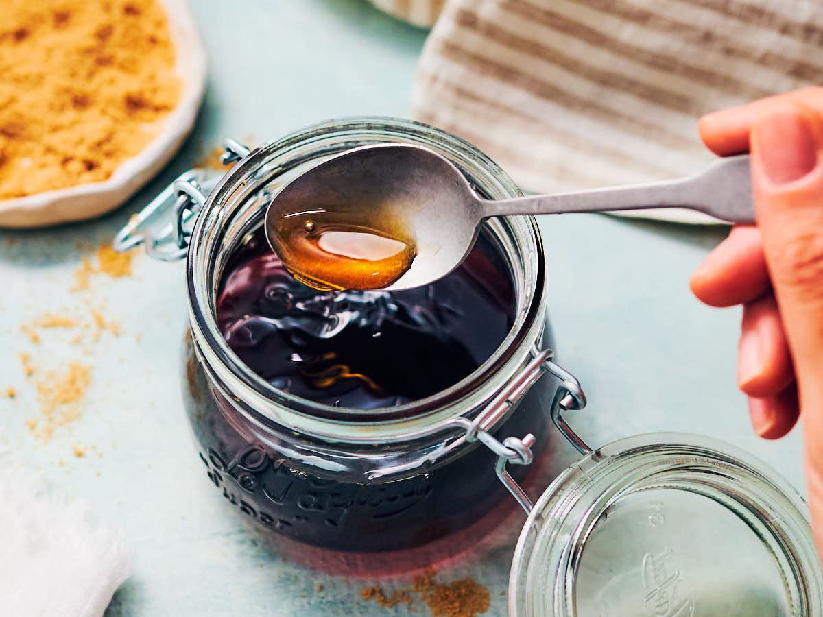 A spoon scooping out brown sugar simple syrup from a glass jar.