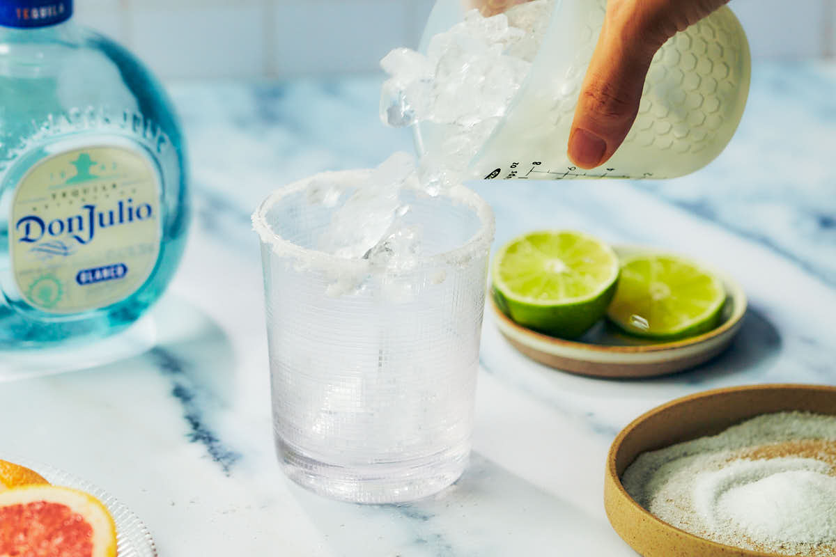 Adding ice to a cocktail glass for grapefruit palomas.