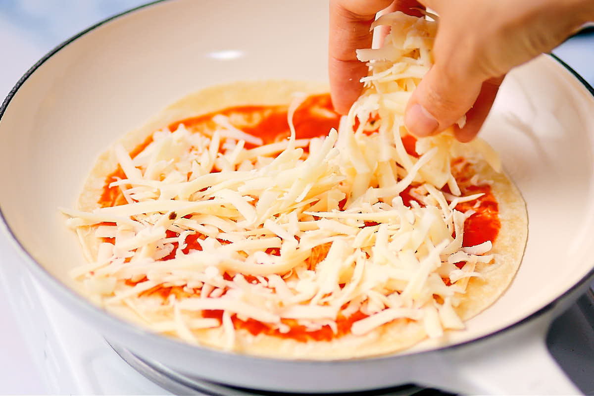 Sprinkling shredded cheese over a tortilla to make cheese quesadillas.
