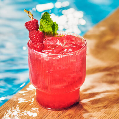 Raspberry Mule in a glass topped with mint and fresh raspberries, by a pool.