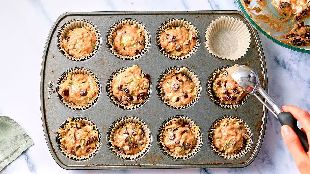 Scooping zucchini muffin batter into a muffin tin before baking.