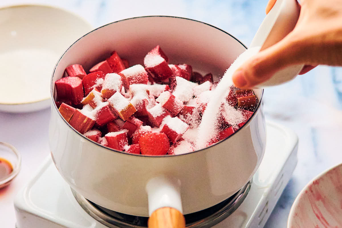 Pouring sugar into a pot of strawberries and rhubarb for compote.