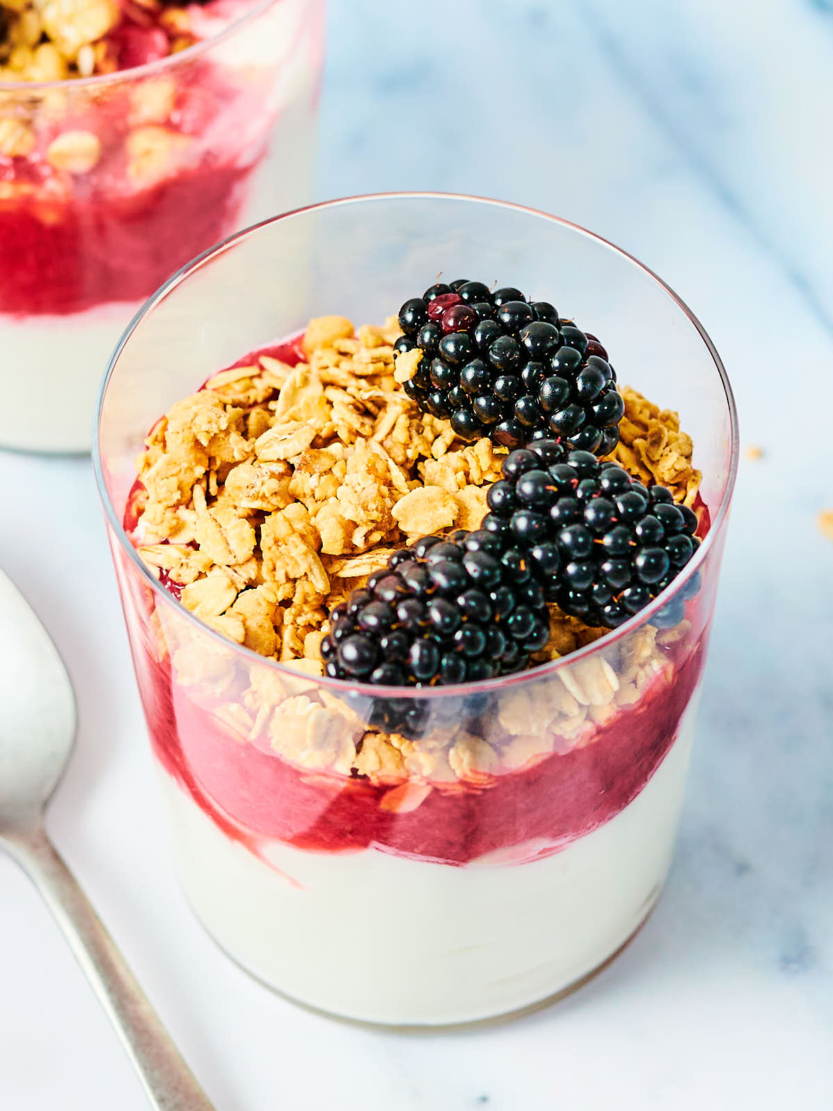 Yogurt, strawberry compote, granola, and berries in a glass cup.