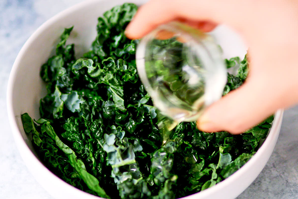 Adding oil and lime juice to kale leaves to marinate.